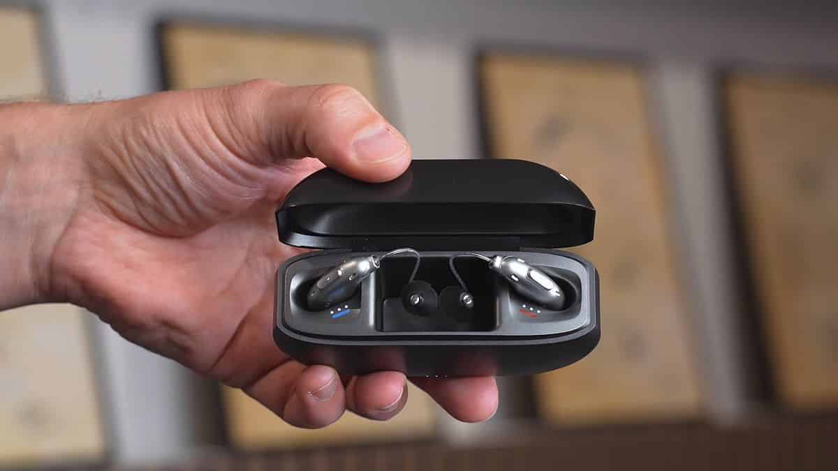 Silver Elehear Beyond Pro in their black open charging case, held by a hand in front of a blurred out background.