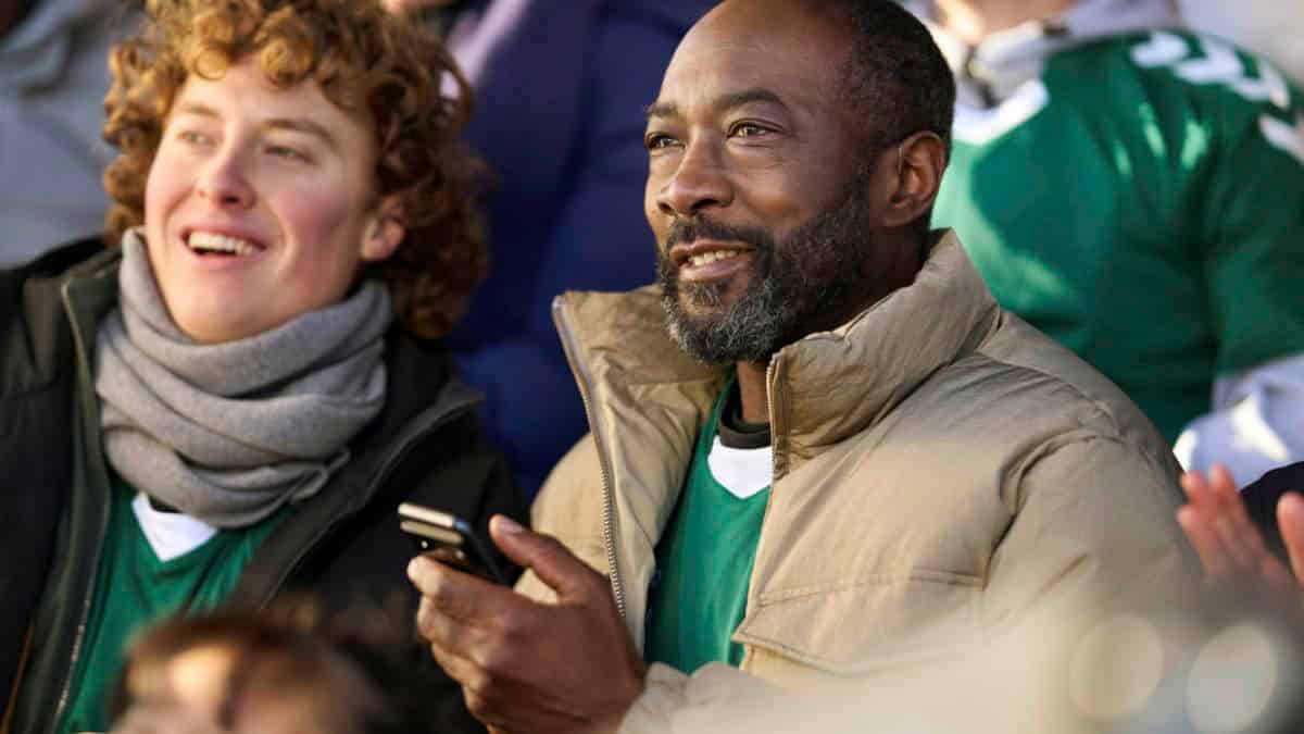 Man with Beltone Serene hearing aids and smartphone at sporting event