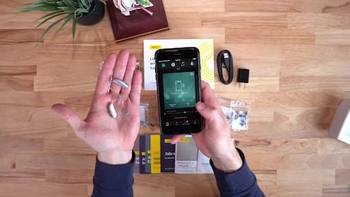 Hands demonstrating a hearing aid and its smartphone app